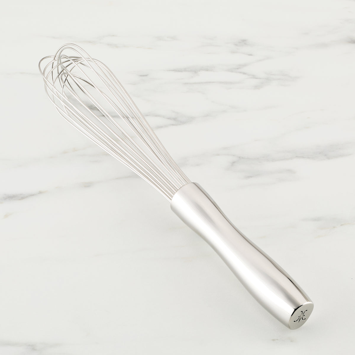 A Hestan Provisions French Whisk with a smooth handle rests on white marble. Made of stainless steel, its long, looped wires converge at the handle, making it ideal for blending and whipping—a must-have in every chefs toolkit.