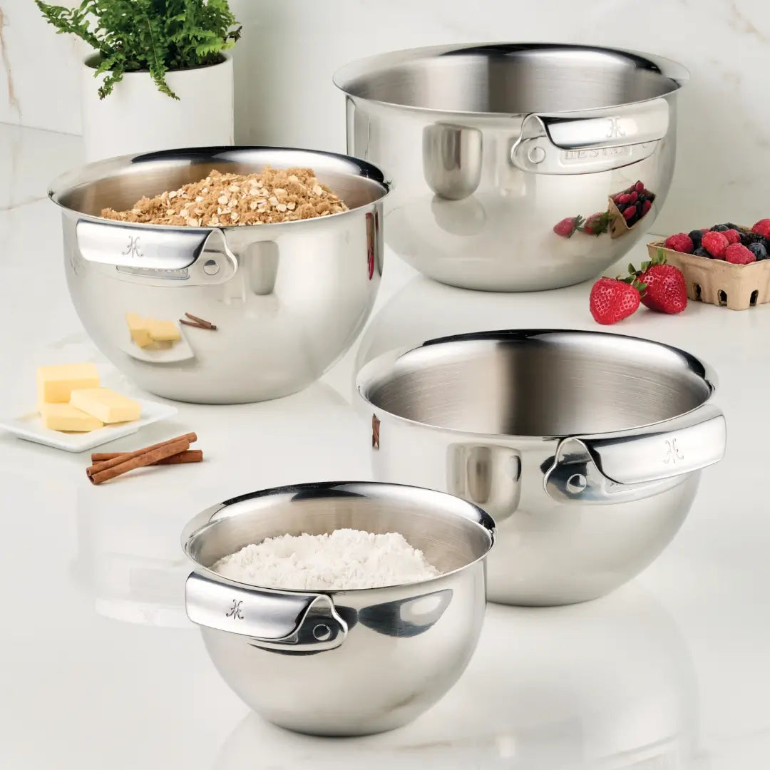 A Hestan Provisions Stainless Steel Mixing Bowl Set, 4-Piece, sits on a white marble countertop. One bowl cradles flour, another oats, and the third holds ripe strawberries. A small tray with butter and cinnamon sticks completes this display of essential kitchenware.