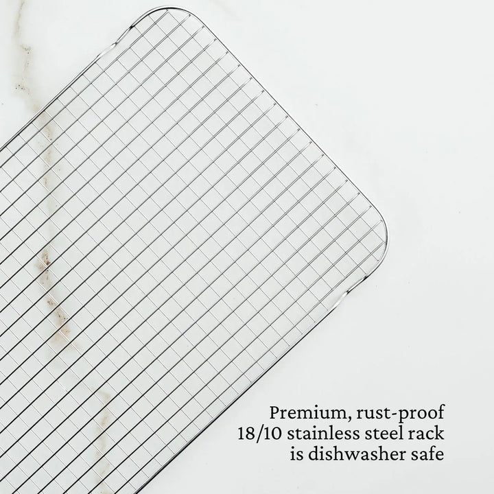 The Hestan Provisions OvenBond Tri-ply Medium Sheet Pan with Rack features a rust-proof 18/10 stainless steel grid-patterned cooling rack on a white marble surface, and the oven-safe sheet pan is triple-bonded clad and dishwasher safe.