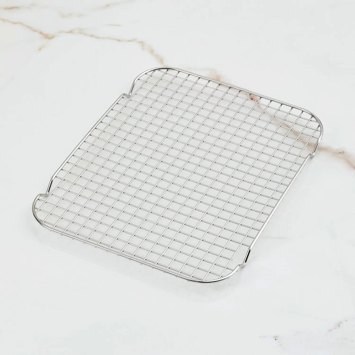 The OvenBond Stainless Steel Medium Pan Rack by Hestan Provisions rests on a white marble surface. With its grid pattern and slightly raised edges, its ideal for cooling baked goods or other foods.