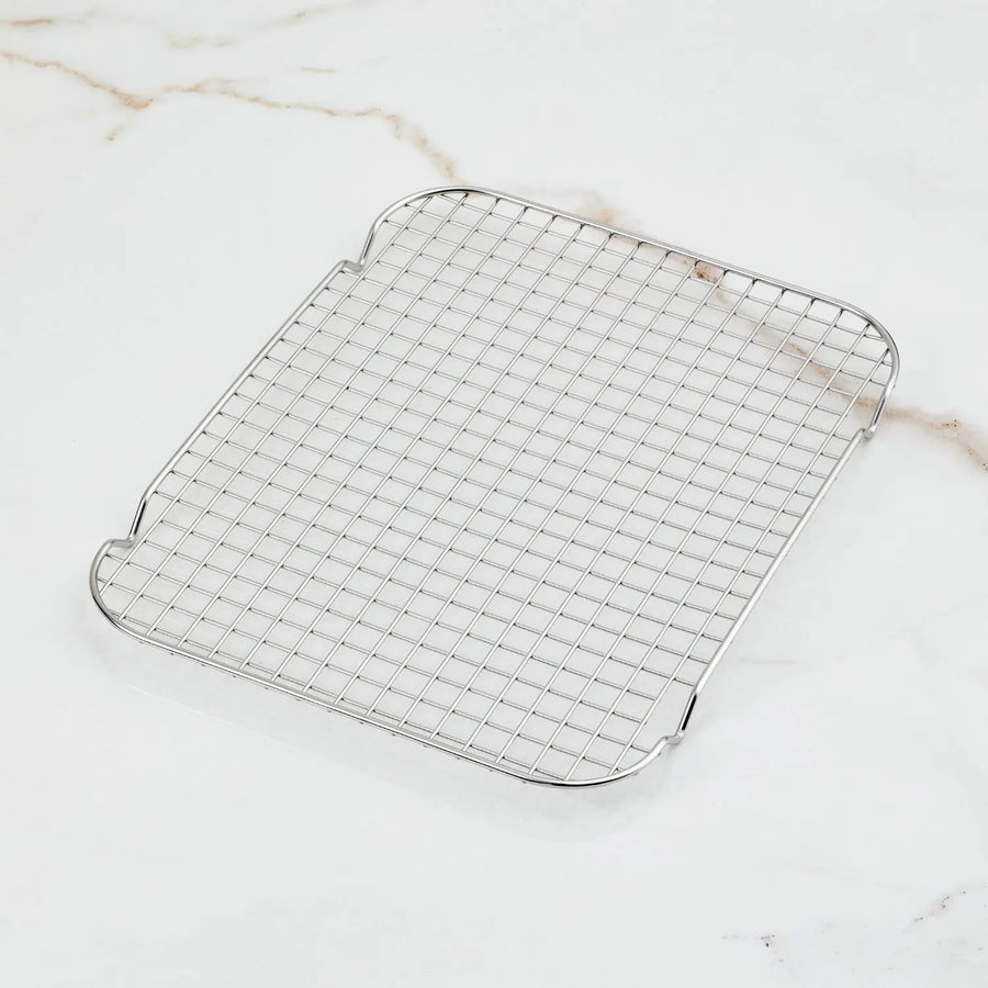 The Hestan OvenBond Tri-Ply Medium Sheet Pan & Rack (12-in x 15-in) features a rectangular grid-patterned rack on a white marble surface with light brown veins, perfectly complementing its premium stainless steel design.
