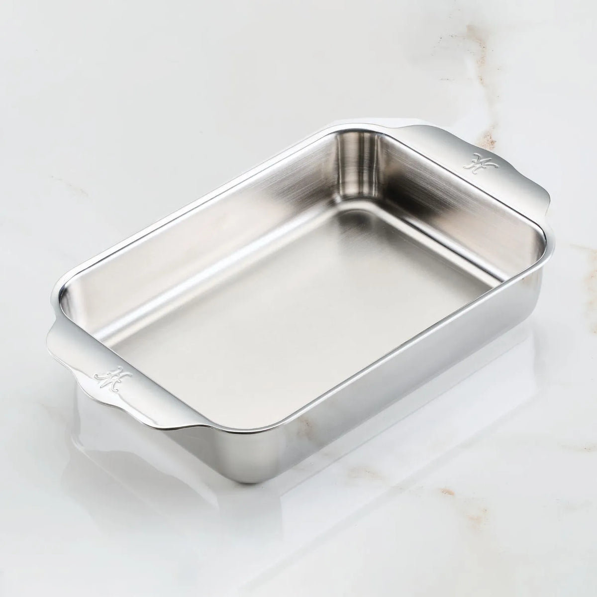 The OvenBond Tri-ply Small Rectangular Baker by Hestan Provisions graces the marble surface with its clad stainless steel design, featuring two subtly embossed handles. Its smooth metal finish combines elegance and sturdiness, ensuring its oven safe.