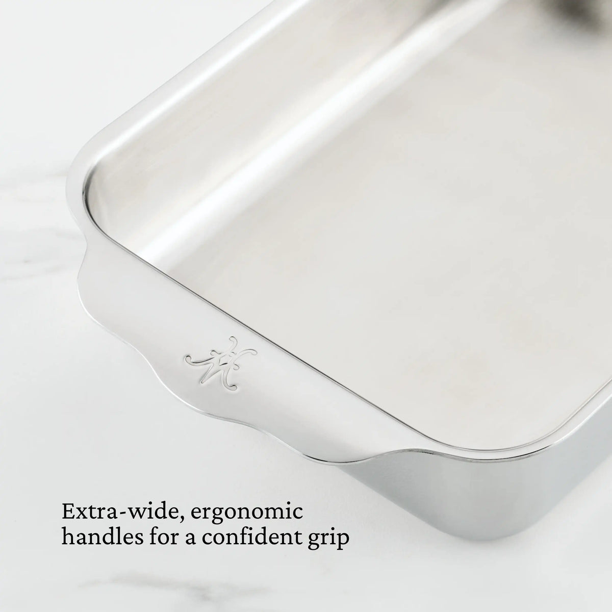 A close-up of the Hestan Provisions OvenBond Tri-ply Small Rectangular Baker with scalloped edges and an engraved emblem. It features extra-wide, ergonomic handles for a confident grip, making it perfect for creating culinary masterpieces and is oven safe.