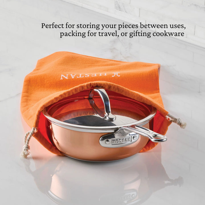 A copper pan with lid rests partially inside an orange Accessories Flannel Cookware Storage Bag on a white surface. Text above notes the bag is ideal for protective cookware storage, travel, or gifting.