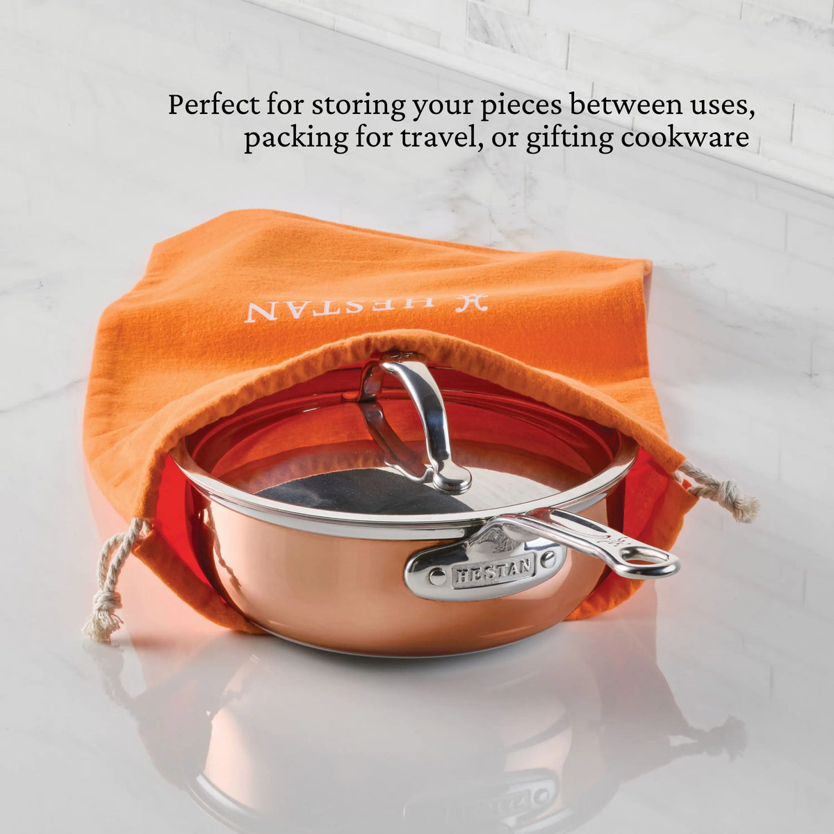 A copper pan with lid rests partially inside an orange Accessories Flannel Cookware Storage Bag on a white surface. Text above notes the bag is ideal for protective cookware storage, travel, or gifting.