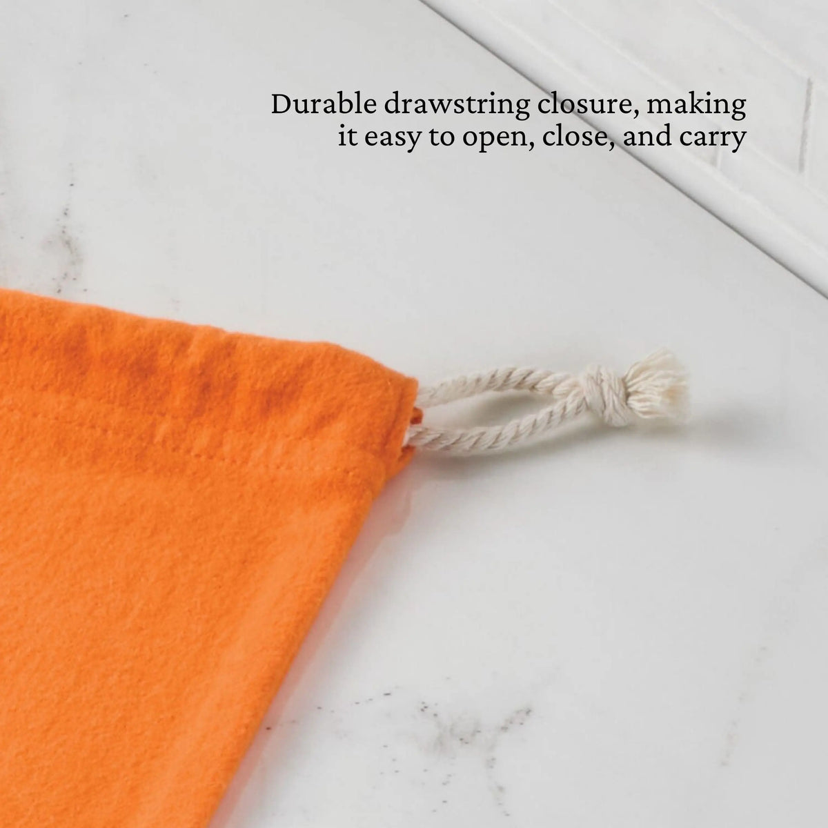The Accessories Flannel Cookware Storage Bag, shown in orange with a white rope drawstring on a marble surface, features a durable closure for easy opening, closing, and carrying.