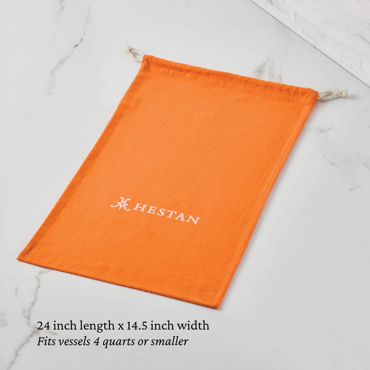 An orange Flannel Cookware Storage Bag by Accessories, featuring a white logo, rests on a marble surface. Measuring 24"x14.5", it's perfect for safely storing vessels up to 4 quarts.