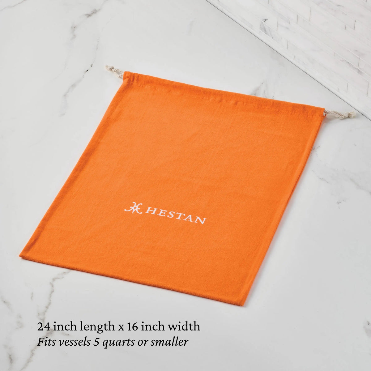 The Accessories Flannel Cookware Storage Bag is an orange drawstring bag with a white Hestan logo, measuring 24" x 16". Perfect for safely storing cookware up to 5 quarts.