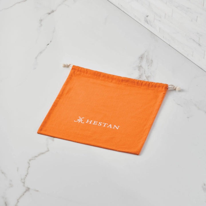 An orange Accessories Flannel Lid Storage Bag lies flat on a white marble surface near a tiled wall, perfect for protecting cookware.