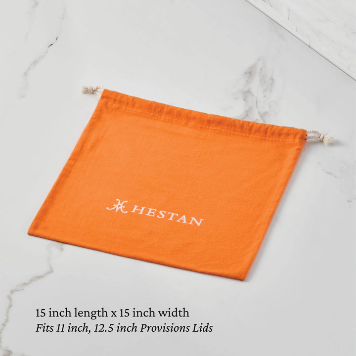 A Flannel Lid Storage Bag by Accessories, orange with HESTAN in white, lies flat on marble. Below: 15" x 15". Ideal for protecting and storing stainless steel lids.