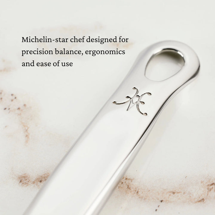 Close-up of a polished metal Fine Mesh Skimmer, 16-inch handle with engraved logo on a light surface. Text overlay: Hestan Provisions—Michelin-star chef designed for precision balance, ergonomics, and ease of use.