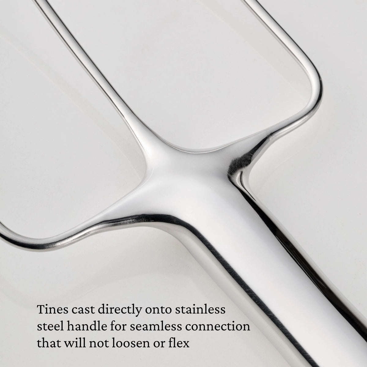 Close-up of a Hestan Provisions® Stainless Steel Carving Fork from the Set of 2, featuring three tines seamlessly cast directly onto the handle. The text highlights this secure, non-flexing connection as a hallmark of professional carving fork durability.