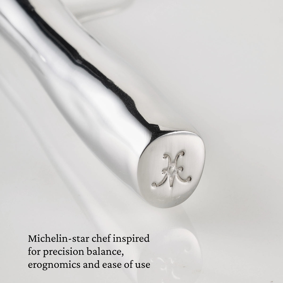 Close-up of a gleaming 18/10 stainless steel handle from a Hestan Provisions® Stainless Steel Carving Fork, Set of 2, finely engraved with a decorative H at the end. Text in the lower left corner reads: Michelin-star chef inspired for precision balance, ergonomics and ease of use—a hallmark of Hestan Provisions® professional carving forks.