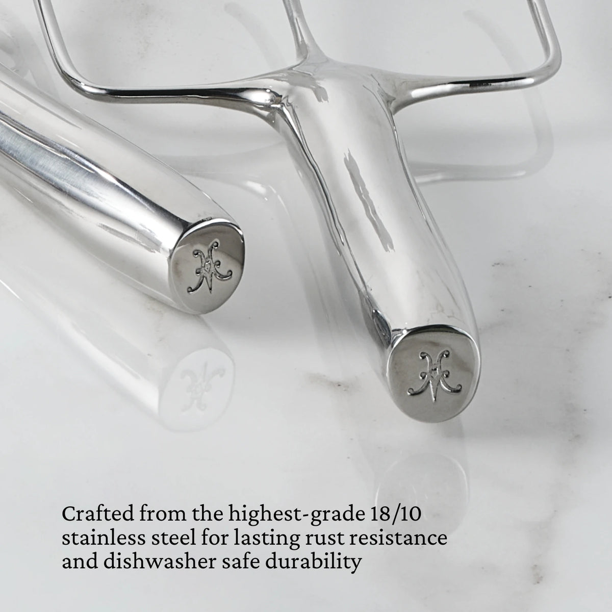 Two Hestan Provisions® Stainless Steel Carving Forks, Set of 2, with engraved handles rest on a white marble surface. Crafted from premium 18/10 stainless steel with a polished finish, these utensils are highlighted by text below for their exceptional rust resistance and dishwasher-safe durability.