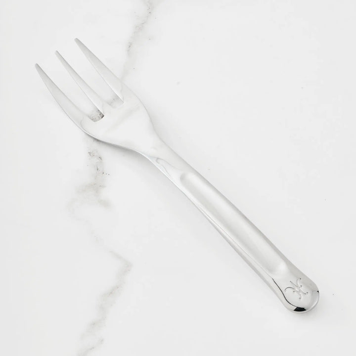 The Hestan Provisions 10.5-inch Stainless Steel Serving Fork, featuring three wide tines and an engraved handle pattern, is part of the Hestan Provisions Serving Tools collection and is shown on a white marble surface—an essential addition to any chef’s kitchen.