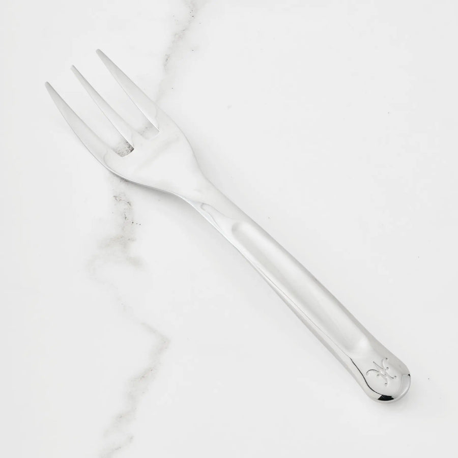 The Hestan Provisions 10.5-inch Stainless Steel Serving Fork, featuring three wide tines and an engraved handle pattern, is part of the Hestan Provisions Serving Tools collection and is shown on a white marble surface—an essential addition to any chef’s kitchen.