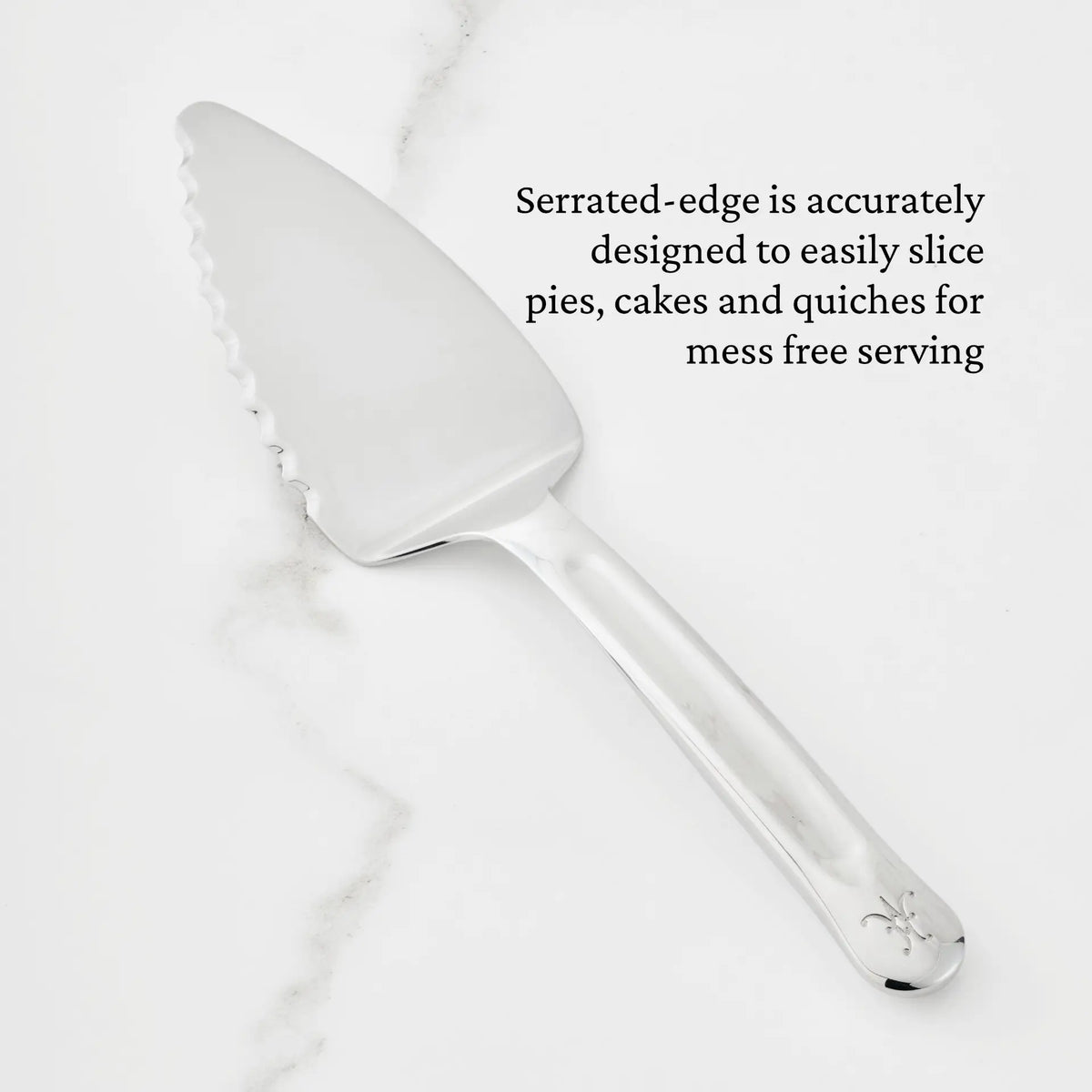 A Hestan Provisions 10.5-inch Stainless Steel Pie & Cake Server, featuring a serrated edge, rests on a white marble surface. Text alongside highlights its thoughtful design for effortlessly slicing pies, cakes, and quiches—making it an essential tool for any chef’s kitchen.