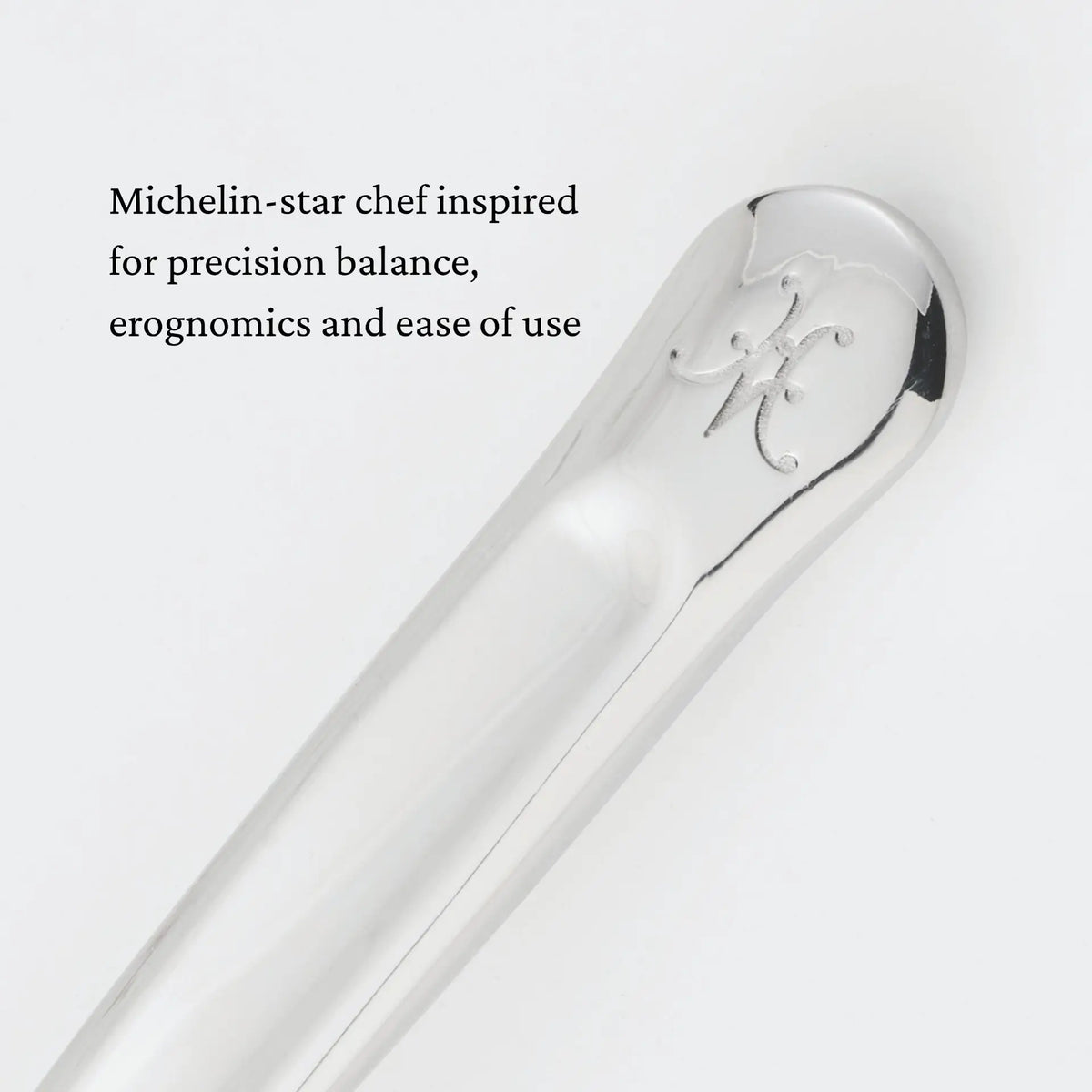 Close-up of a polished metal utensil handle engraved with the letter M. Black text on a white background reads: Michelin-star chef inspired for precision balance, ergonomics and ease of use—crafted to meet the demands of a chef’s kitchen, like the Hestan Provisions 10.5-inch Stainless Steel Pie & Cake Server.