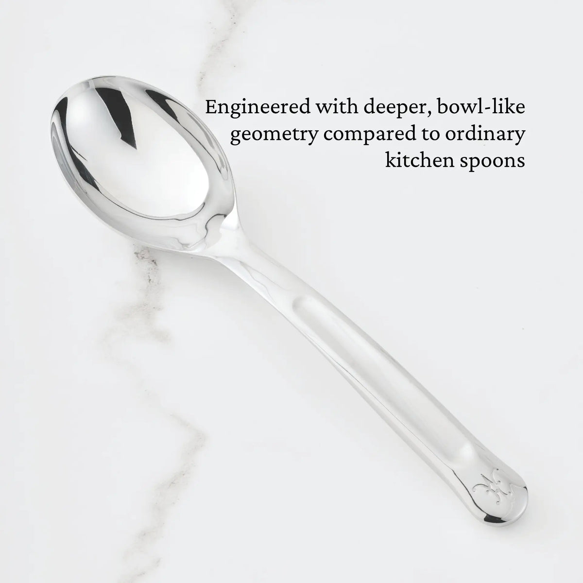 A gleaming 10.5-inch Stainless Steel Solid Serving Spoon from the Hestan Provisions collection rests on a white marble surface. Text above highlights, Engineered with deeper, bowl-like geometry compared to ordinary kitchen spoons—an essential addition to your chef’s tools and part of the Hestan Provisions Serving Tools collection.