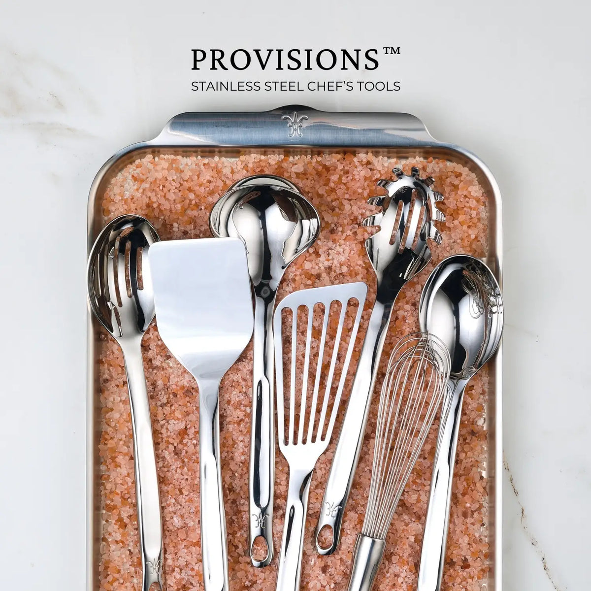 The Hestan Provisions™ Slotted Turner, 13-inch, crafted from durable 18/10 stainless steel, is pictured on pink Himalayan salt with the text above reading PROVISIONS™ Stainless Steel Chefs Tools.