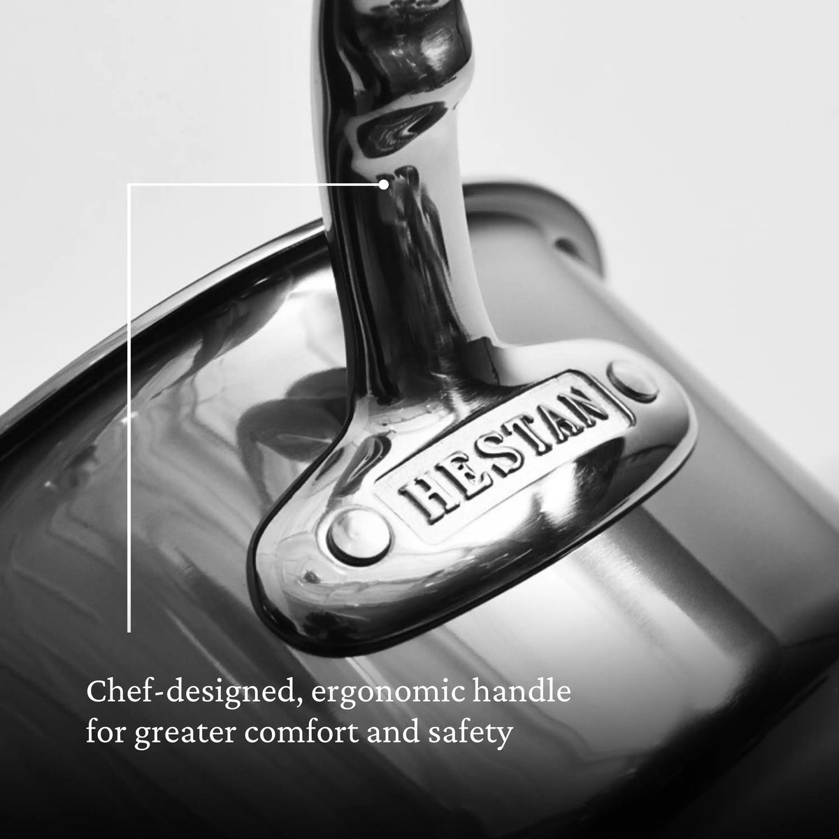 Close-up of a Titanium Saucepan showcases its shiny, silver handle engraved with HESTAN, emphasizing NanoBonds ergonomic design. White text reads: Chef-designed, ergonomic handle for enhanced comfort and safety.