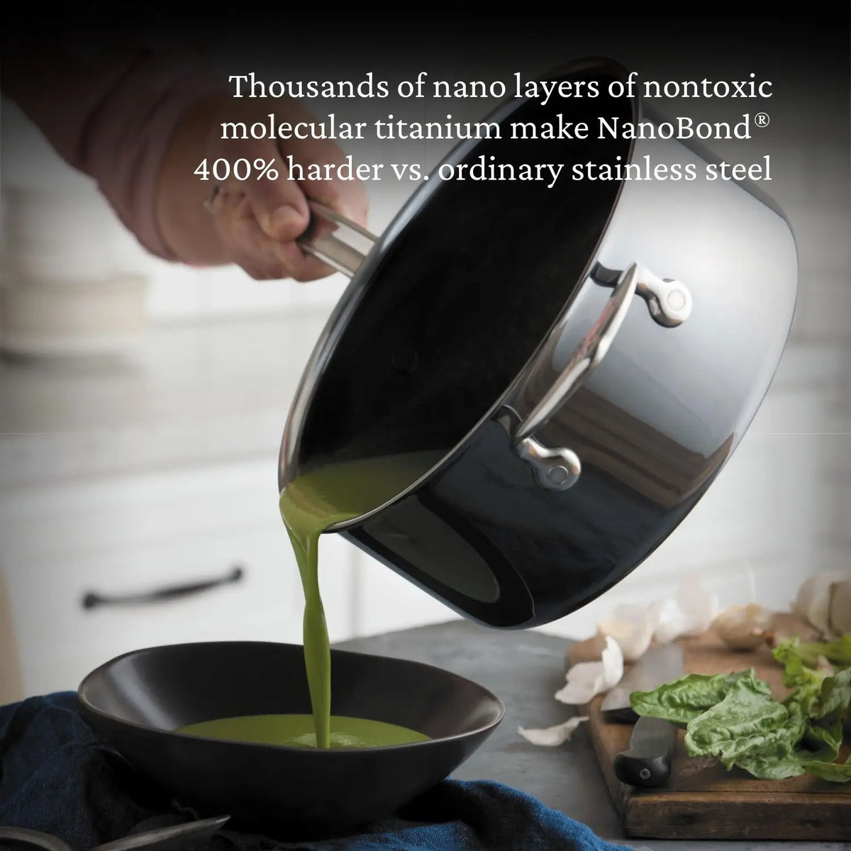 A hand pours green soup from a NanoBond Titanium Saucepan into a black bowl. The text overlay highlights its NanoBond Molecular Titanium, noted to be 400% harder than stainless steel. Metal utensil safe, its perfect for your kitchen adventures. Lettuce and garlic are on the countertop.
