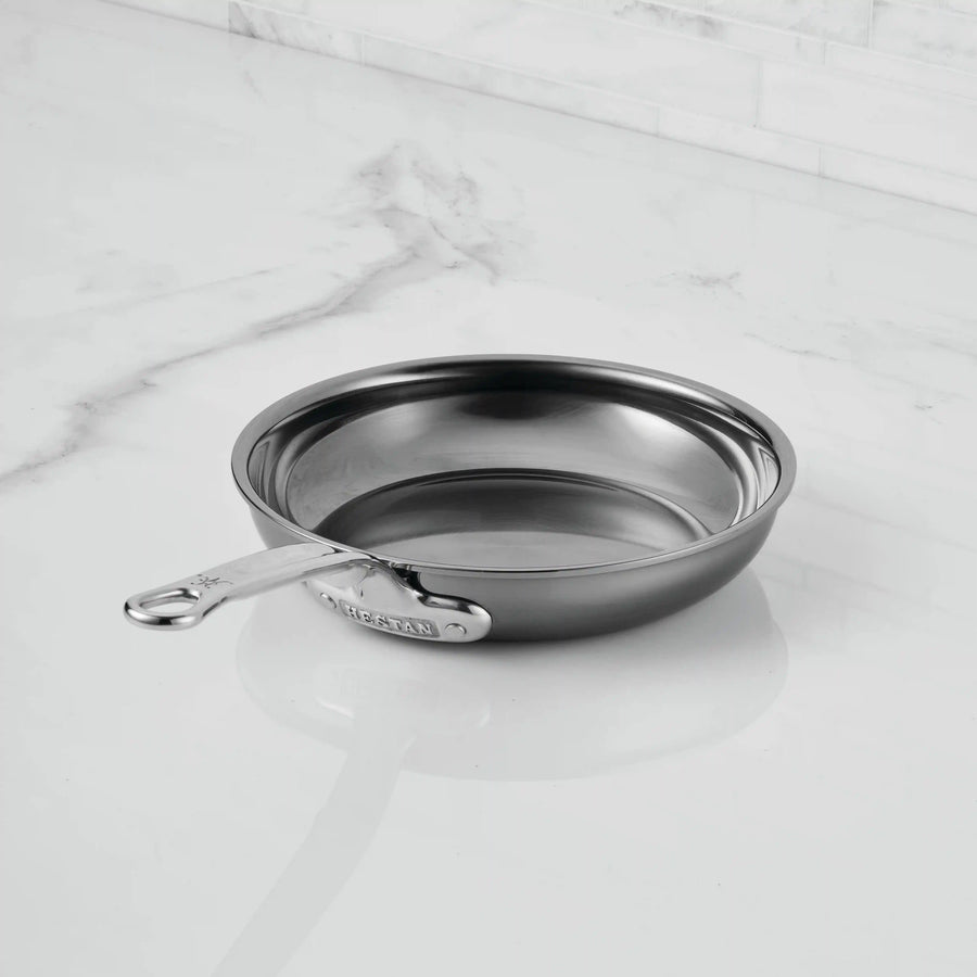 A clean NanoBond Titanium Skillet with a metal handle sits on a white marble countertop. This nonreactive pan ensures superior cooking performance, and its reflective surface adds to the tidy look of the area.
