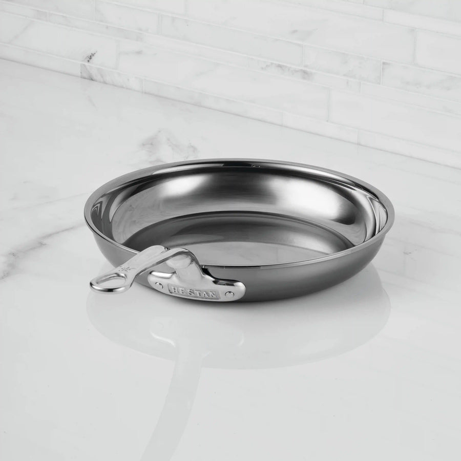 A NanoBond Titanium Skillet with a shiny finish and straight handle sits on a white marble countertop, highlighting its nonreactive titanium construction against the white tile backsplash.