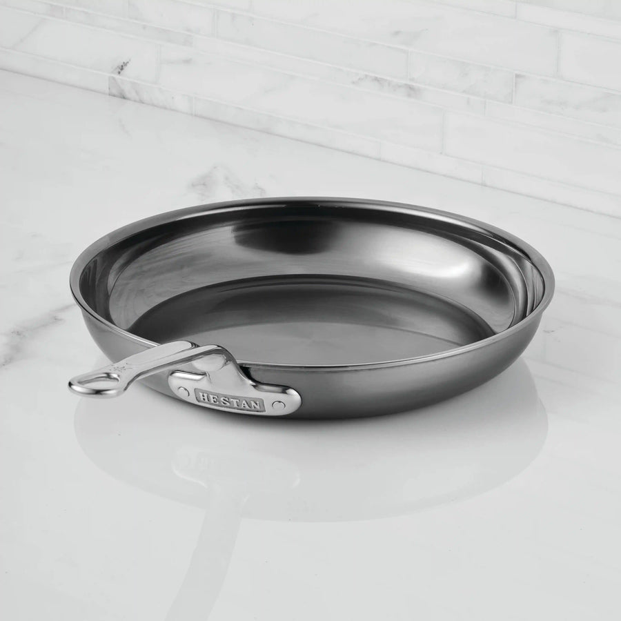 A NanoBond Titanium Skillet with a stainless finish and metal handle sits on a white marble countertop, backed by a white tiled backsplash.