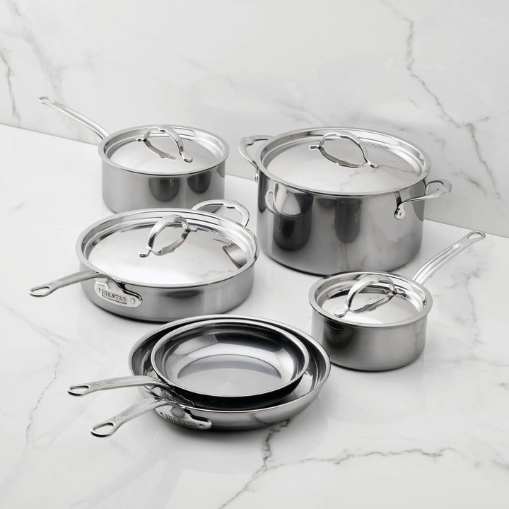 The NanoBond 10-Piece Titanium Ultimate Cookware Set, featuring frying pans, saucepans with lids, a sauté pan with lid, and a stockpot with lid, is displayed on a white marble countertop with a marble backsplash.