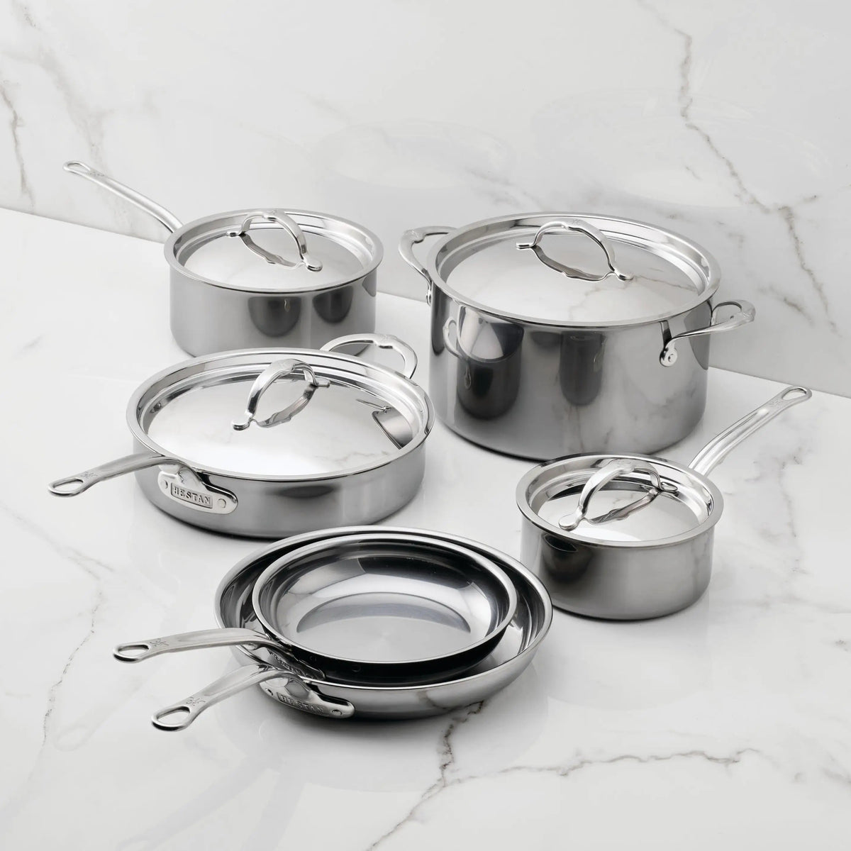 The NanoBond 10-Piece Titanium Ultimate Cookware Set, featuring frying pans, saucepans with lids, a sauté pan with lid, and a stockpot with lid, is displayed on a white marble countertop with a marble backsplash.