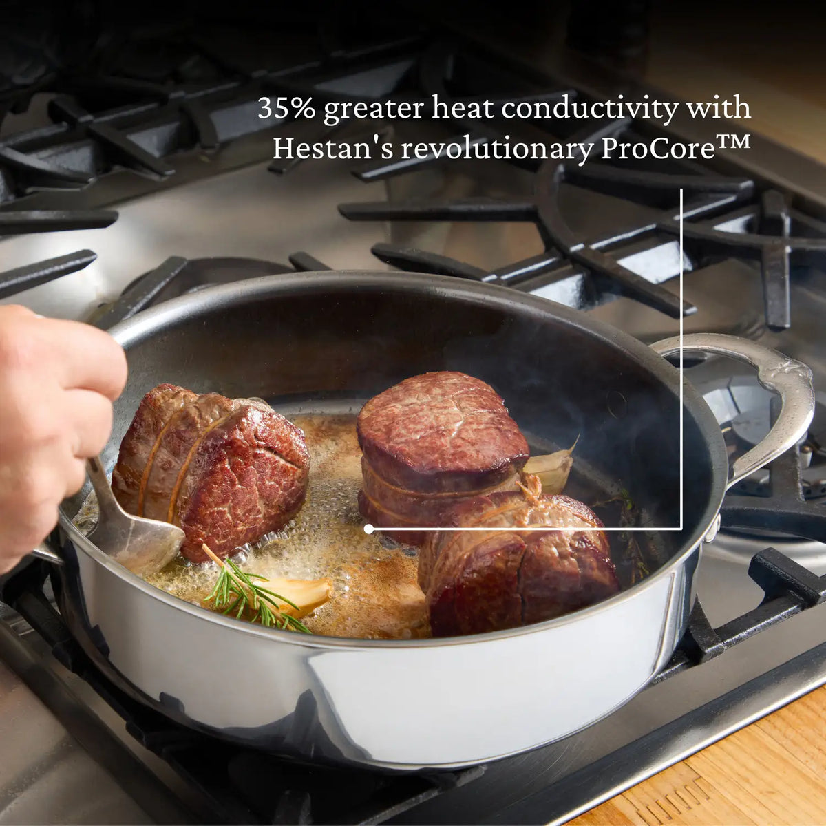 A hand expertly sears steak medallions in a NanoBond Titanium Sauté Pan on a gas stove. Enhanced with rosemary sprigs, the stainless steel pan features ProCore technology for 35% more heat conductivity and molecular titanium durability.