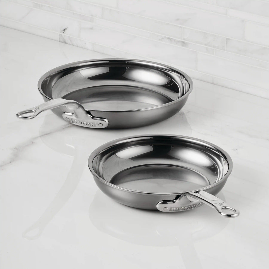 Two NanoBond Titanium Skillets with handles, including a premium titanium skillet, rest on a white marble countertop in a kitchen with a white tiled backsplash.