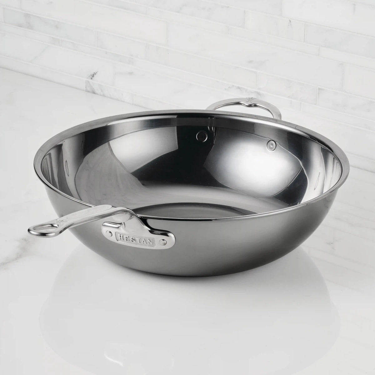 A NanoBond Titanium Chefs Pan, 14-inch, with two handles sits on a white marble countertop against a white tile backsplash.