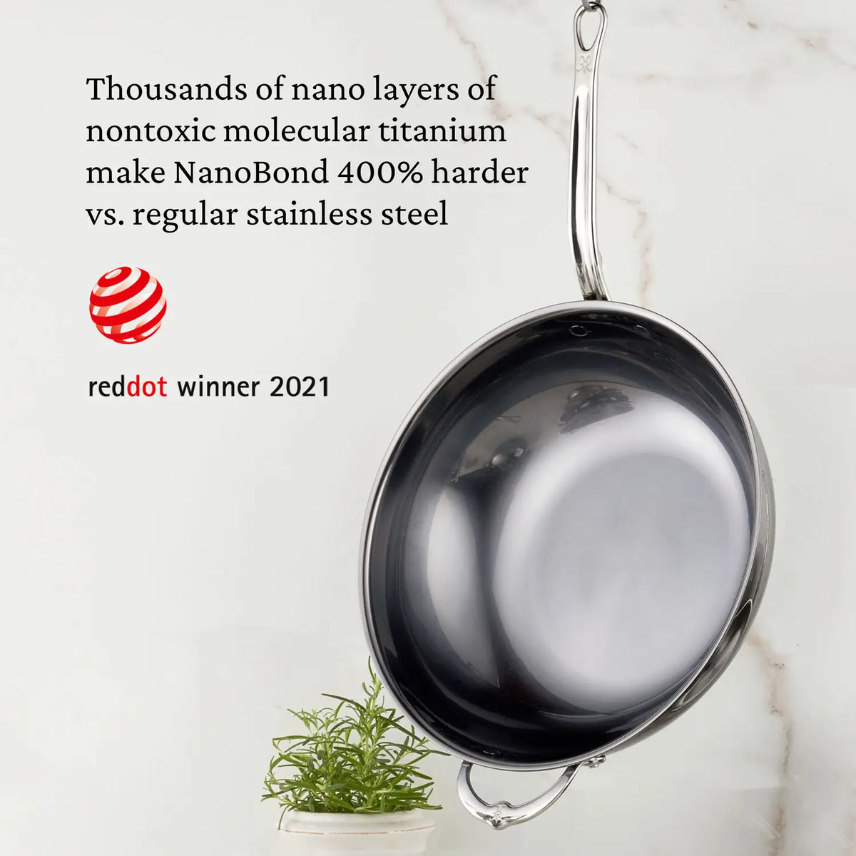 A 14-Inch Titanium Chefs Pan by NanoBond hangs against a marble backdrop, crafted with nontoxic titanium nano layers making it 400% harder than regular stainless steel. Featured is the prestigious Red Dot Award winner 2021 logo.
