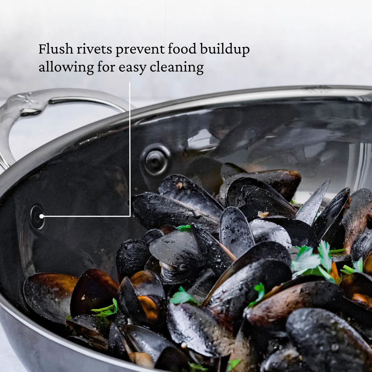 A close-up of mussels inside a 14-Inch Titanium Chefs Pan by NanoBond shows flush rivets with text overlay: Flush rivets prevent food buildup for easy cleaning. Parsley garnishes the mussels, highlighting its molecular titanium finish.
