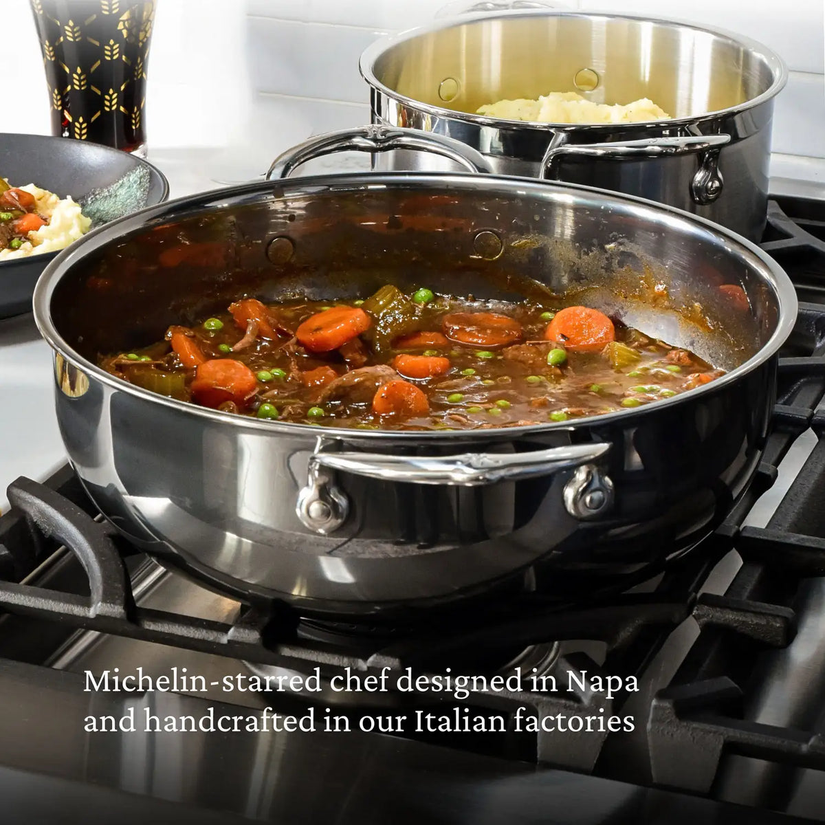 A NanoBond Titanium Dutch Oven, 5-Quart, rests on a stovetop containing a stew with carrots and peas. Another pan with white rice is in the background. Text reads: Michelin-starred chef designed in Napa and handcrafted in our Italian factories.