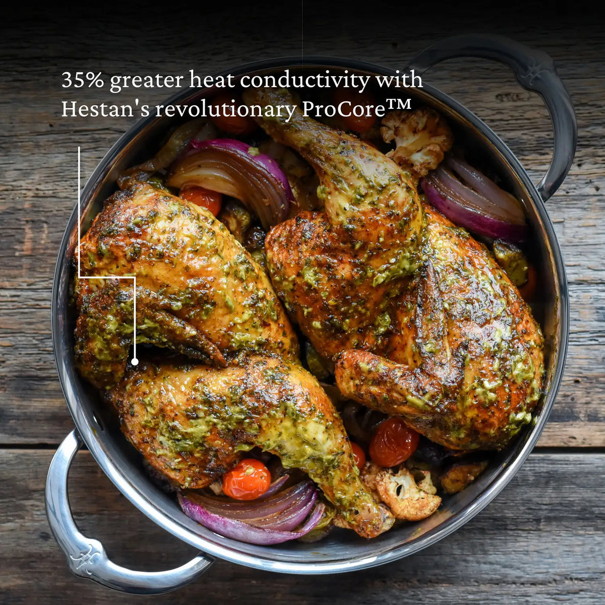 A 5-quart Titanium Dutch Oven by NanoBond filled with roasted chicken, herbs, red onion slices, cherry tomatoes, and cauliflower. Text: 35% greater heat conductivity with Hestan NanoBonds revolutionary ProCore™.