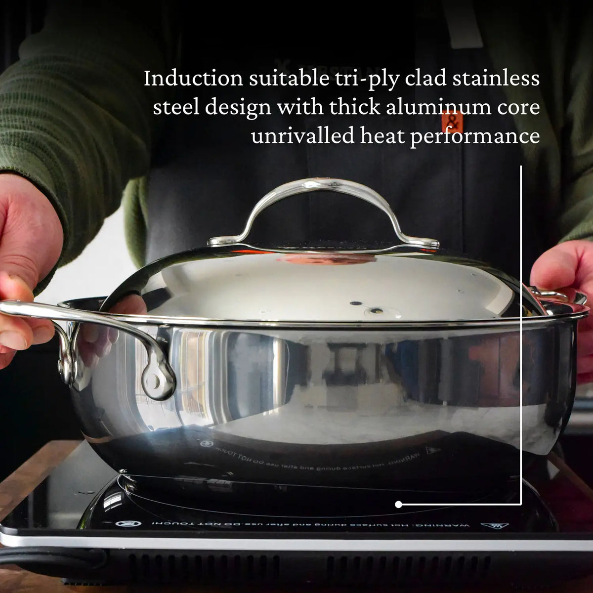 Wearing a black apron, a person holds a pot from the NanoBond 10-Piece Limited Edition Titanium Cookware Set over an induction cooktop, showcasing its tri-ply stainless steel, thick aluminum core, and NanoBond Molecular Titanium for superior heat performance.
