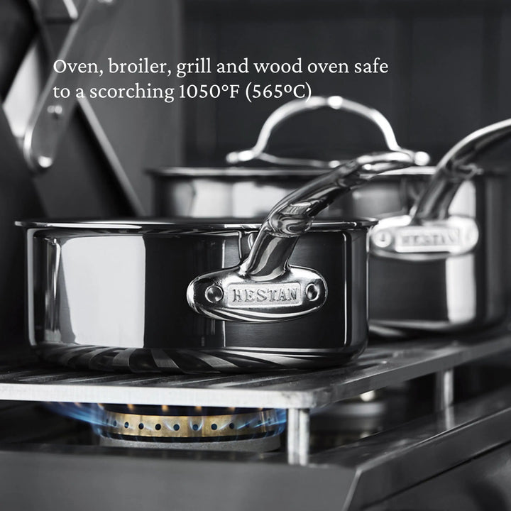 Two Titanium Stockpots by NanoBond sit on a gas burner with a blue flame. Text above states: Oven, broiler, grill, and wood oven safe up to a scorching 1050°F (565°C).