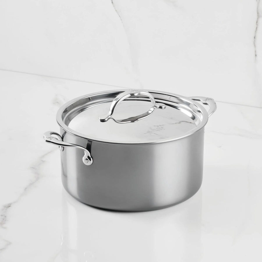 A NanoBond Titanium Stockpot with dual handles and a matching lid rests on a white marble countertop, showcasing its reflective finish and sleek, modern style.