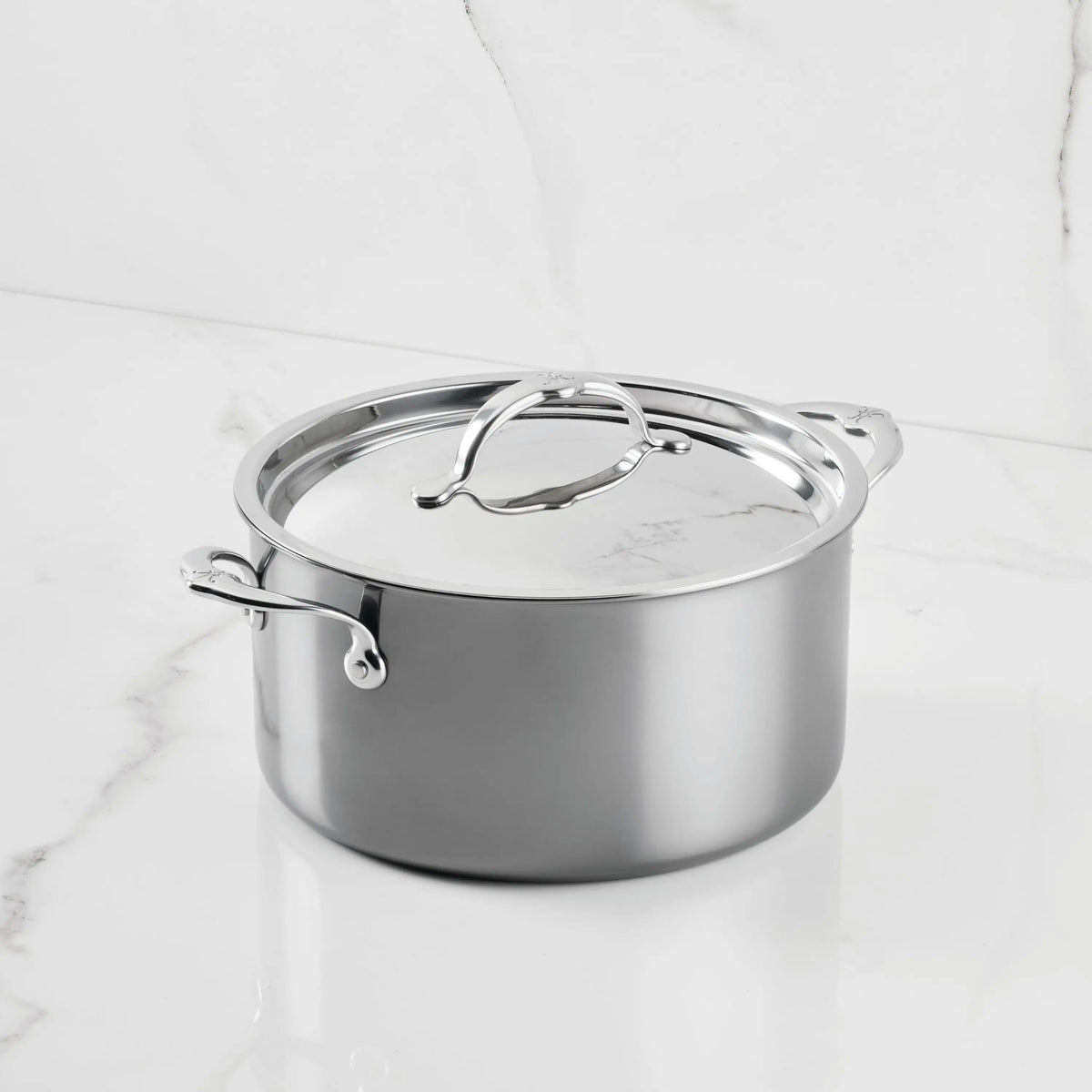 A NanoBond Titanium Stockpot with dual handles and a matching lid rests on a white marble countertop, showcasing its reflective finish and sleek, modern style.