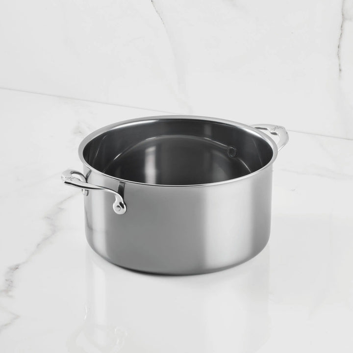 A NanoBond Titanium Stockpot with two handles sits on a white marble countertop, its empty, spotless surface gleaming—a signature of this advanced molecular titanium cookware.