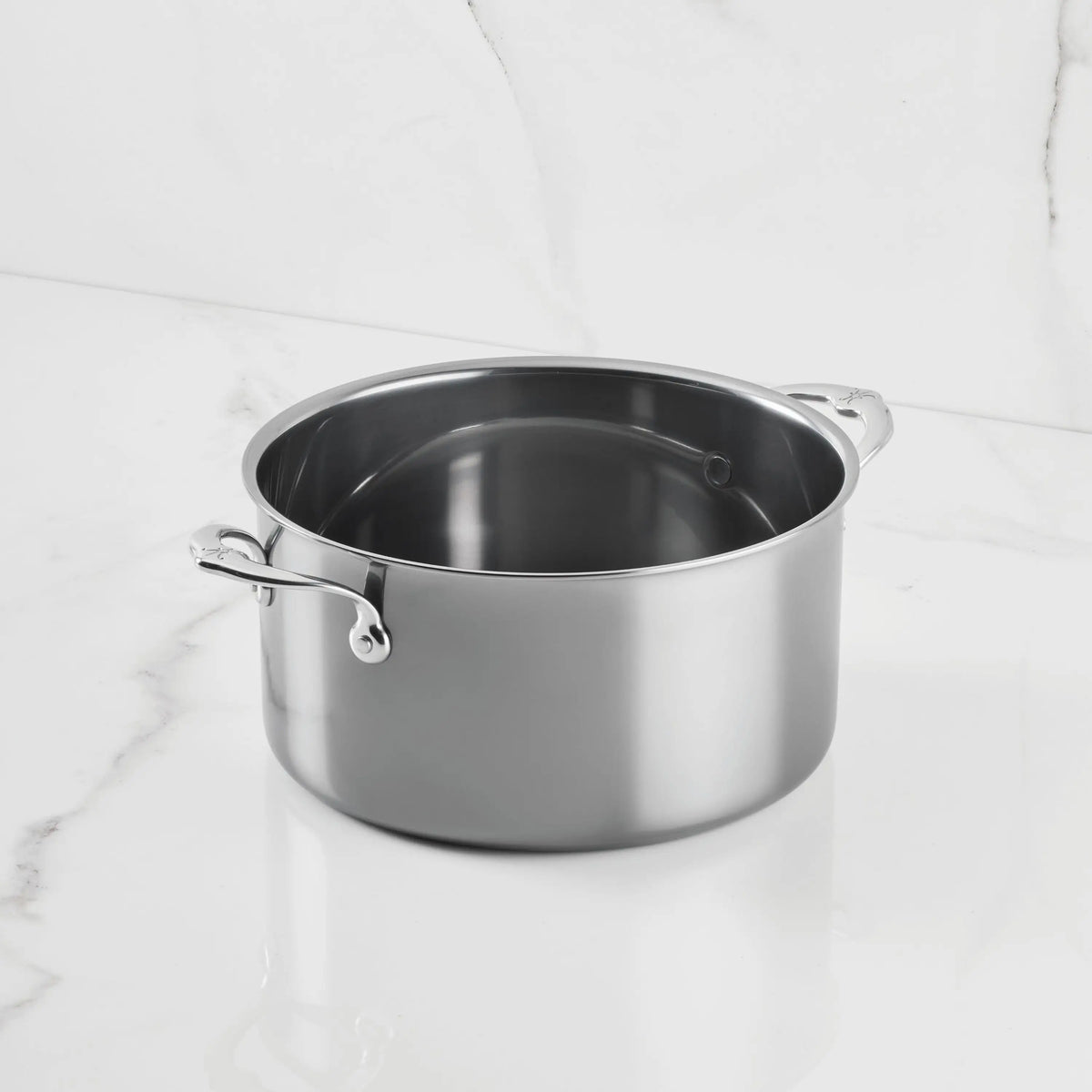 A NanoBond Titanium Stockpot with two handles sits on a white marble countertop, its empty, spotless surface gleaming—a signature of this advanced molecular titanium cookware.