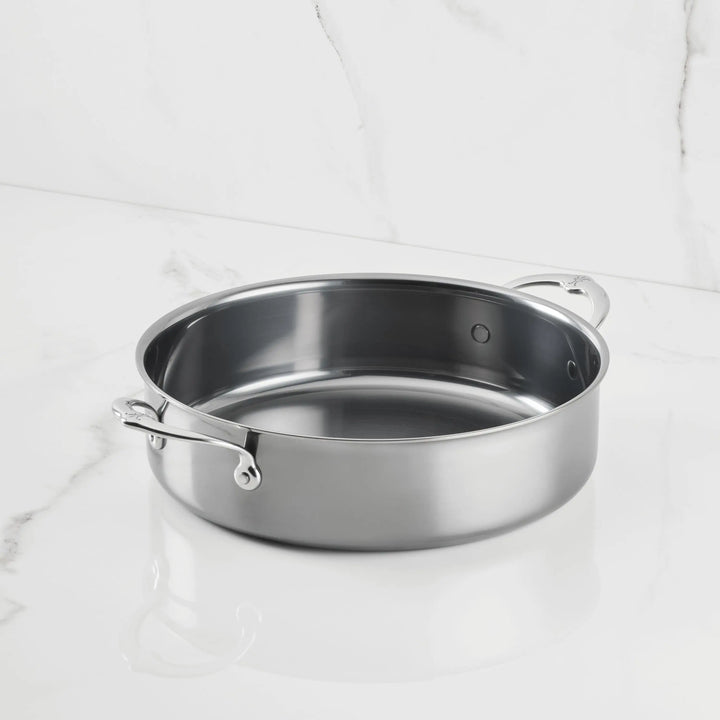 A NanoBond Titanium Rondeaus sauté pan with dual side handles, featuring advanced technology, is displayed on a white marble surface against a matching marble background.