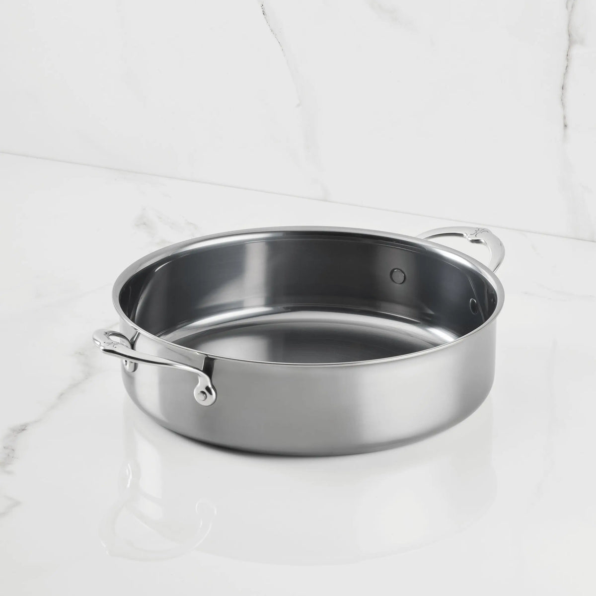 A NanoBond Titanium Rondeaus sauté pan with dual side handles, featuring advanced technology, is displayed on a white marble surface against a matching marble background.
