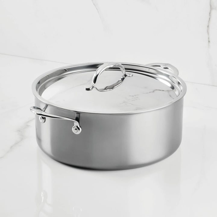 The NanoBond Titanium Rondeaus, featuring metal handles and a matching lid, sit on a white marble countertop—ideal for versatile cooking.