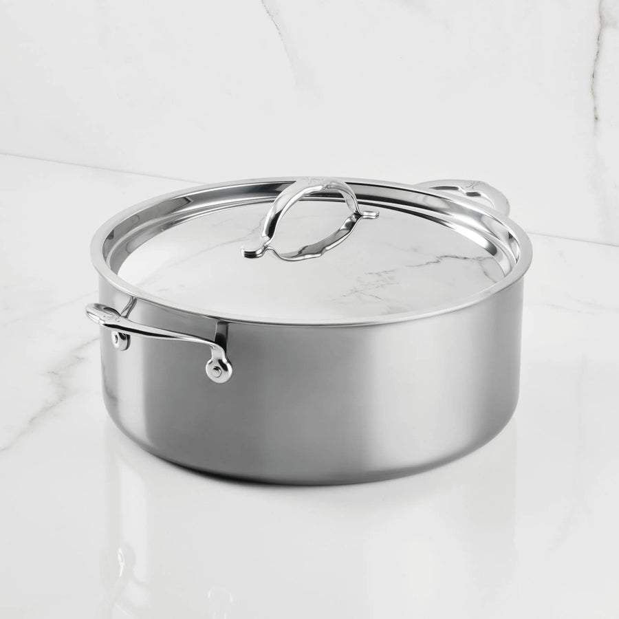 The NanoBond Titanium Rondeaus, featuring metal handles and a matching lid, sit on a white marble countertop—ideal for versatile cooking.