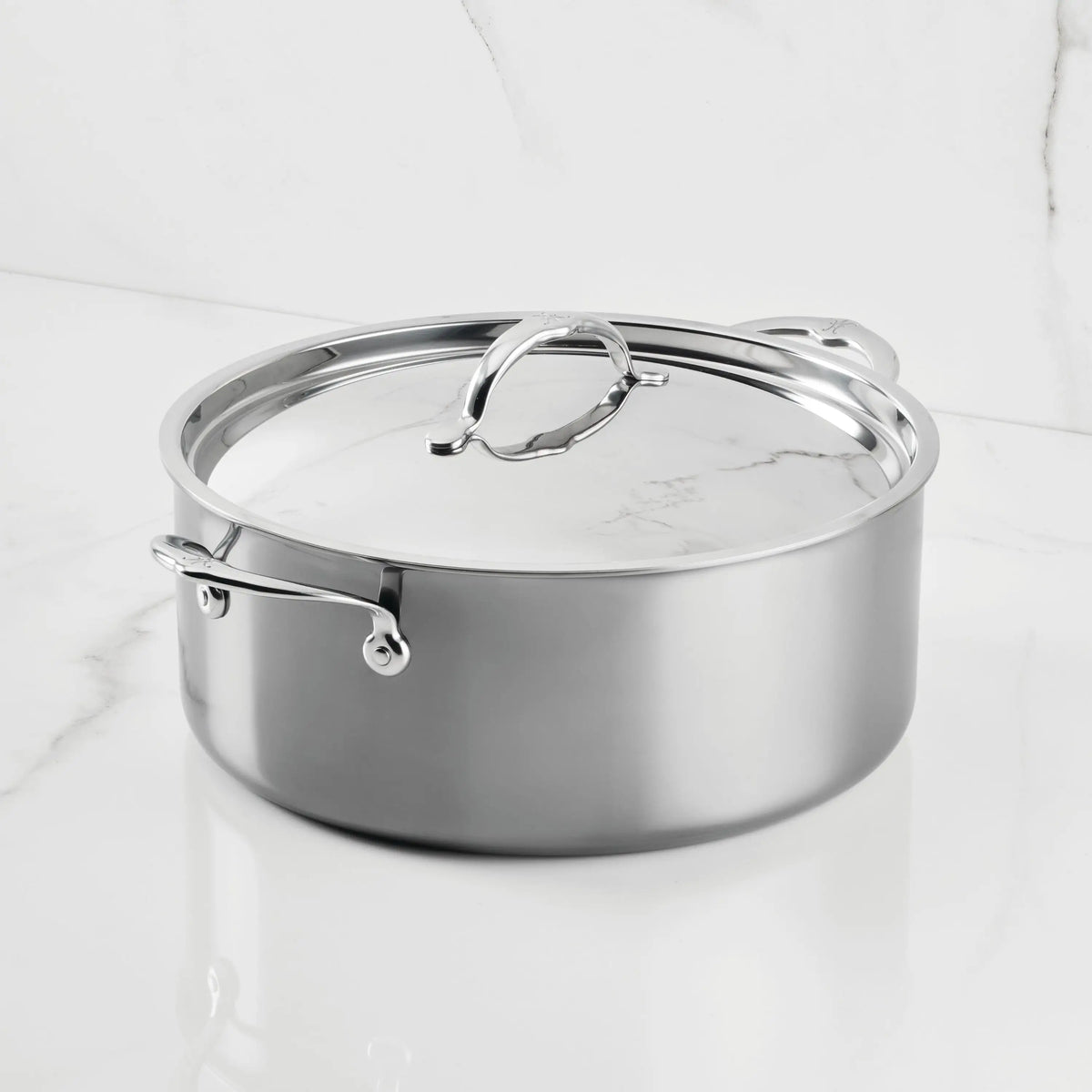 The NanoBond Titanium Rondeaus, featuring metal handles and a matching lid, sit on a white marble countertop—ideal for versatile cooking.