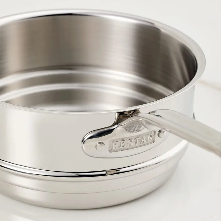 Close-up of a Hestan Provisions Stainless Steel Double Boiler Insert, 3-Quart, showcasing even heat distribution. Its shiny surface features a handle with visible rivets and an engraved brand name on a metallic plate, set against a plain light-colored background.